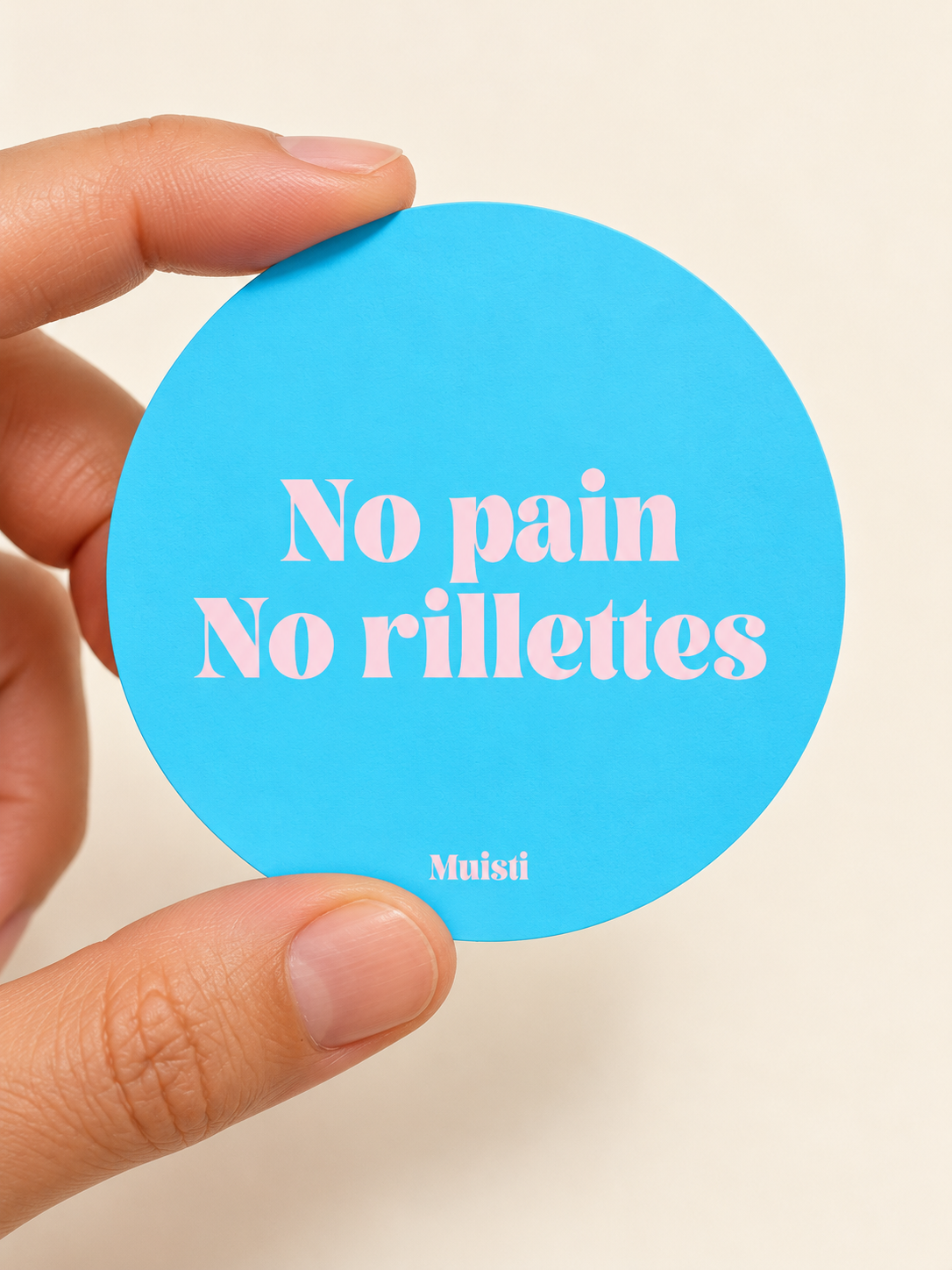 Sticker Muisti No pain No rillettes tenu entre le pouce et l’index sur fond ivoire