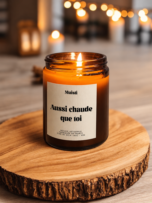 Bougie Muisti « Aussi chaude que toi » allumée, en pot ambré sur un socle en bois.