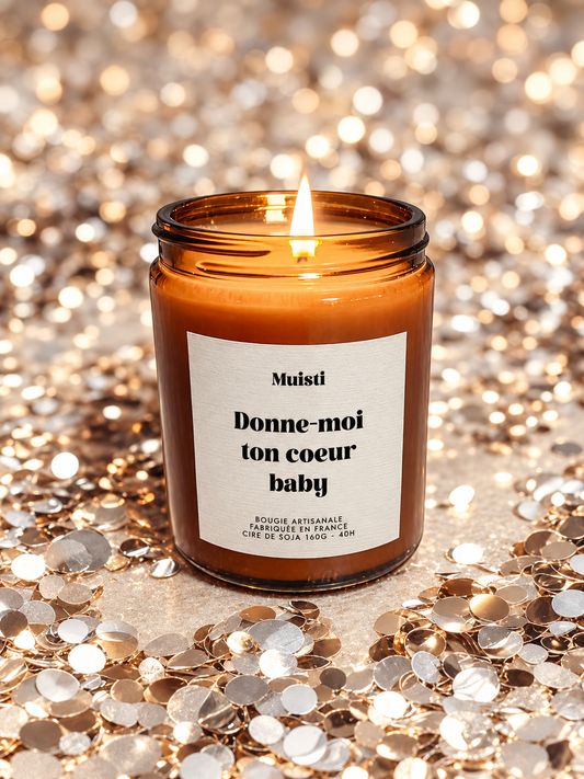 Bougie Muisti « Donne-moi ton cœur baby » allumée, en pot ambré avec une étiquette texturée, entourée de confettis.