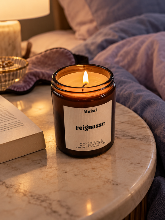 Bougie Muisti « Feignasse » allumée sur une table de chevet, en soirée.