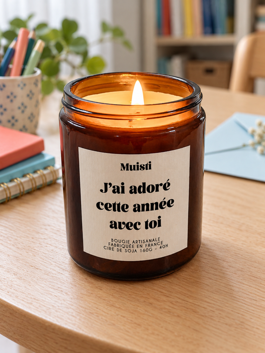 Bougie Muisti « J'ai adoré cette année avec toi » 160 g allumée dans un intérieur à la lumière douce du jour.