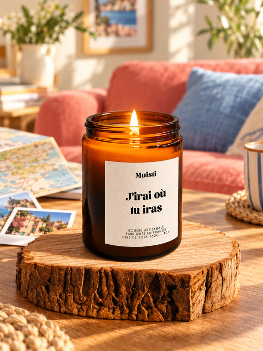 Bougie Muisti « J’irai où tu iras » allumée dans un salon coloré avec des souvenirs de voyage.