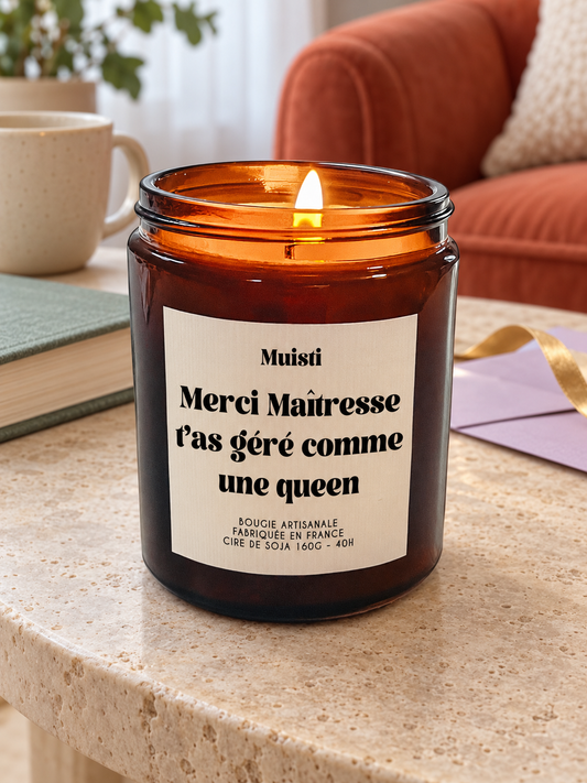 Bougie Muisti « Merci Maîtresse, t'as géré comme une queen » 160 g allumée sur une table dans un intérieur à la lumière douce du jour.