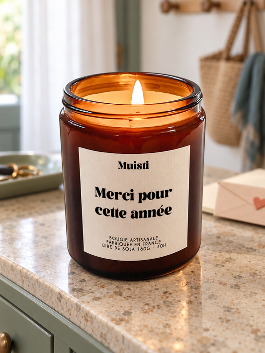 Bougie Muisti « Merci pour cette année » 160 g allumée dans un intérieur à la lumière douce du jour.