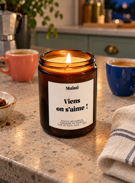 Bougie Muisti « Viens on s’aime ! » allumée sur un comptoir de cuisine, en soirée.