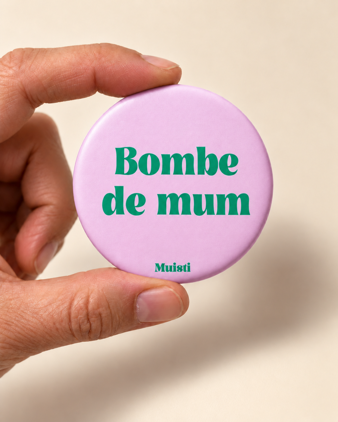 Magnet Muisti « Bombe de mum » tenu entre le pouce et l’index sur fond ivoire.